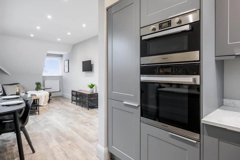Modern kitchen with grey cabinetry, stainless steel built-in appliances and open-plan living area