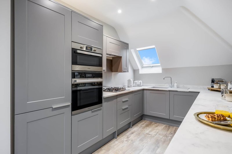 Modern gray kitchen with built-in appliances, white countertops, skylight window and wooden flooring