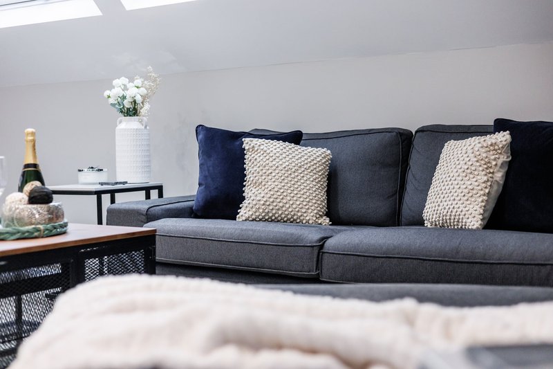 Modern living room with grey sofa, navy and cream cushions, white flowers, and champagne bottle