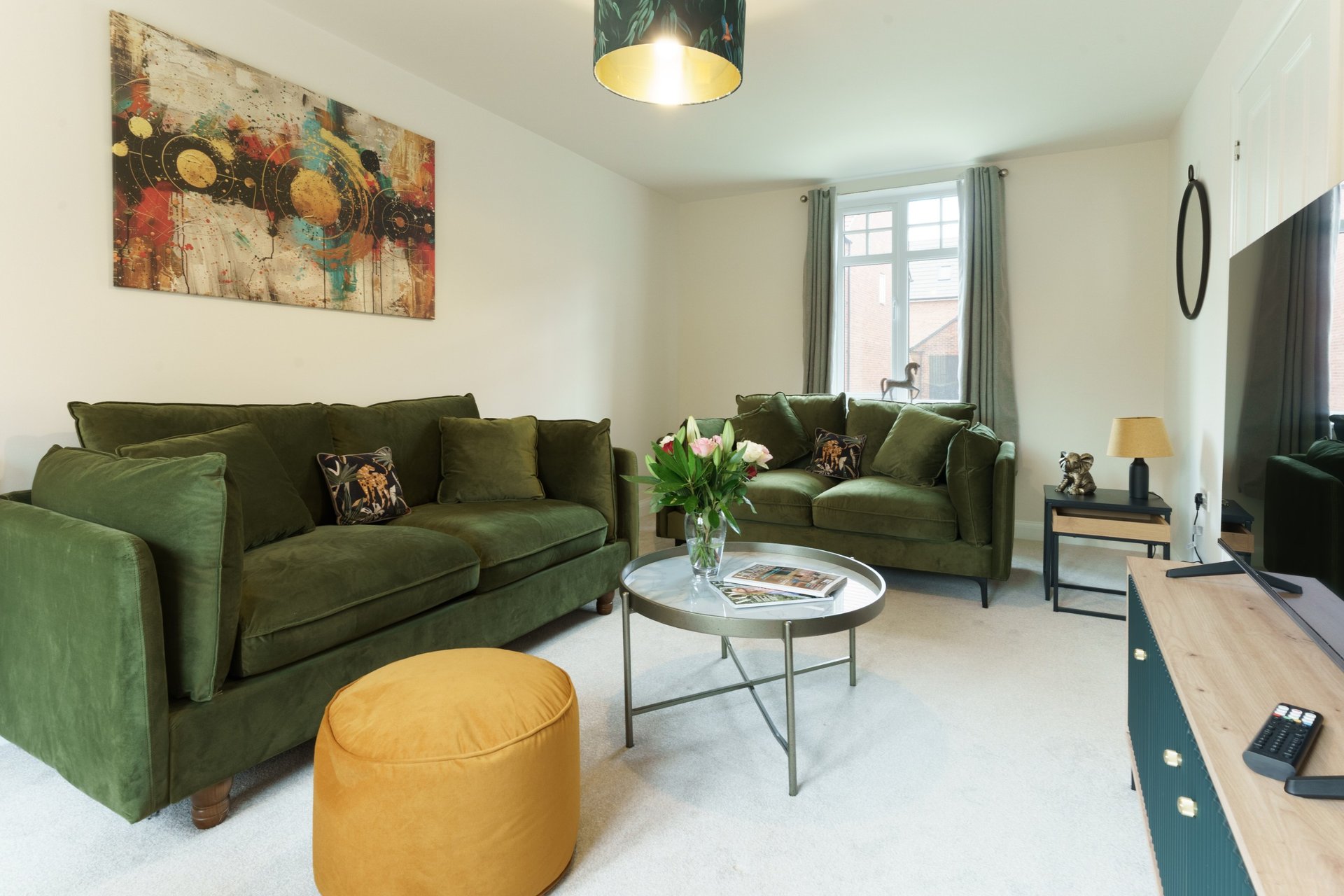 Bright living room with green sofas, yellow ottoman, glass coffee table and wall art