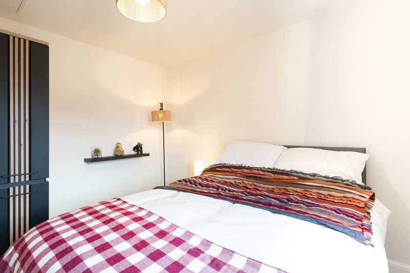 Bright bedroom with two single beds, striped blankets, wall shelf and floor lamp