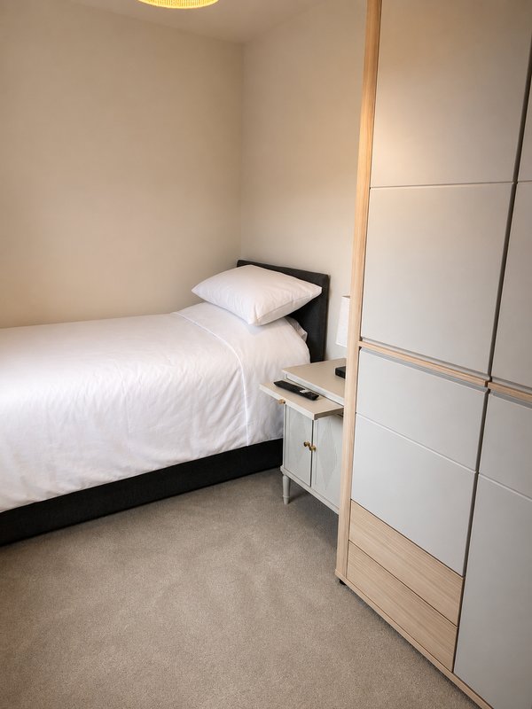 Small bedroom with single bed, white bedding, black frame, and built-in wardrobe