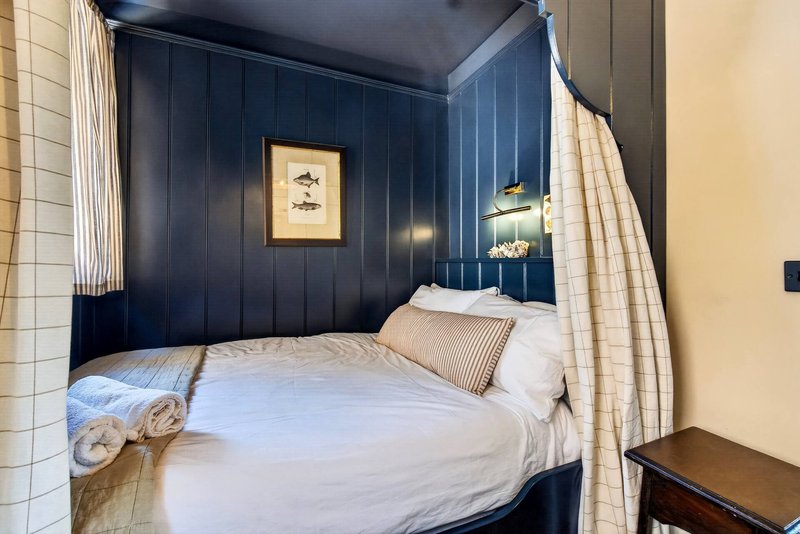 Bedroom with four-poster bed, dark blue paneled walls, striped curtains and framed artwork