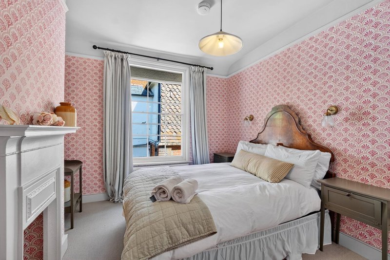 Bedroom with double bed, pink patterned wallpaper, pendant light and window with curtains