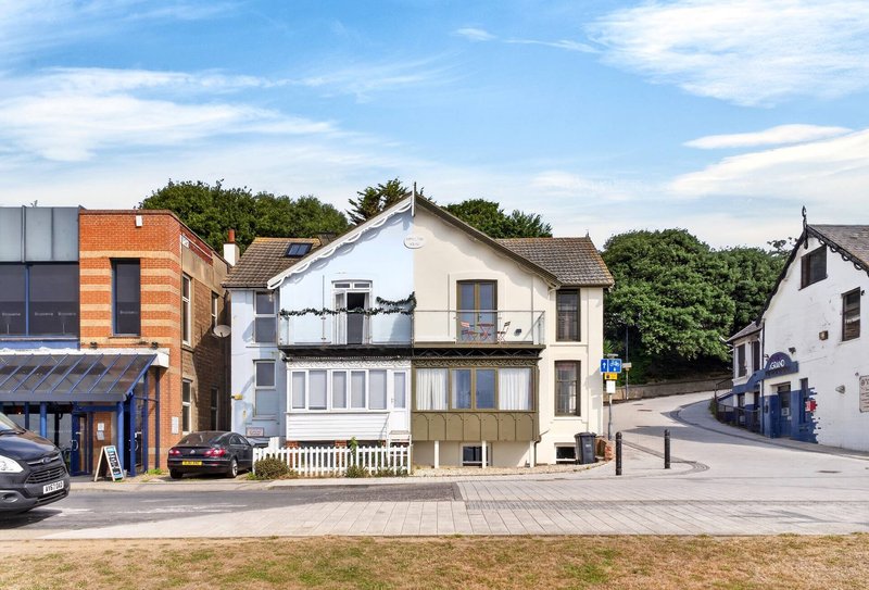 Street view of white-painted residential building with adjoining brick extension and parked vehicles