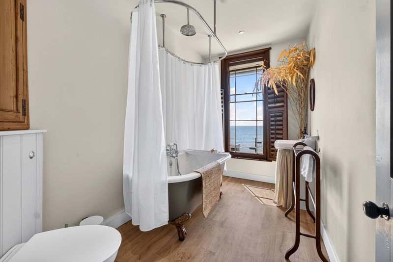 Bathroom with freestanding bathtub, shower enclosure, toilet, and window with coastal view