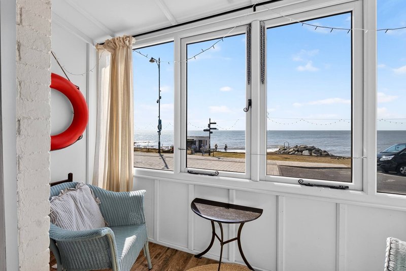 Bright room with large windows overlooking beach, red life preserver on wall, seating area