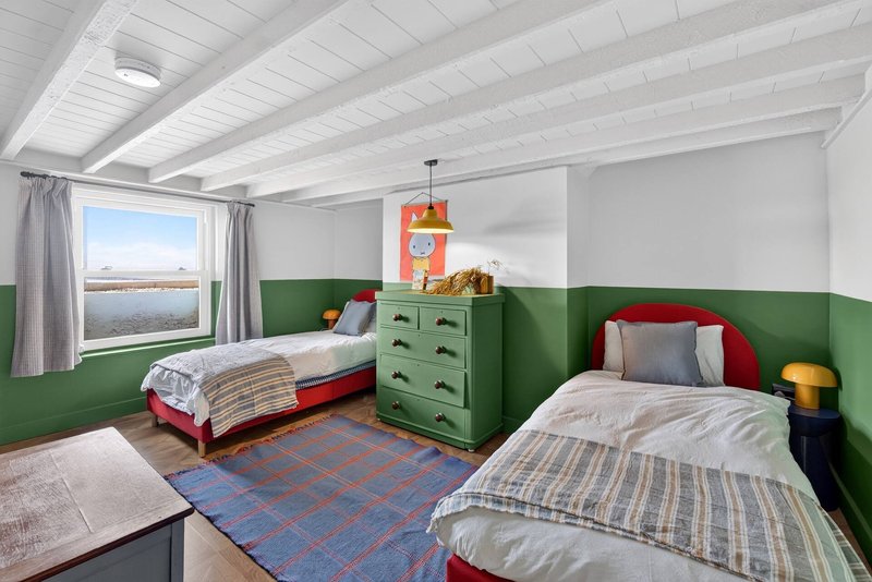 Bright twin bedroom with white ceiling, green half-painted walls, two beds, green dresser, window with water view
