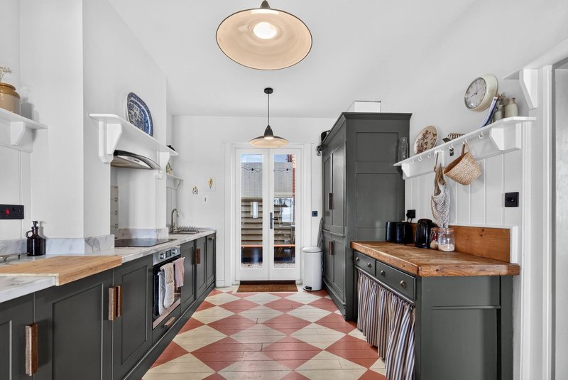 Modern kitchen with dark cabinetry, wooden countertops, geometric floor tiles and pendant lighting