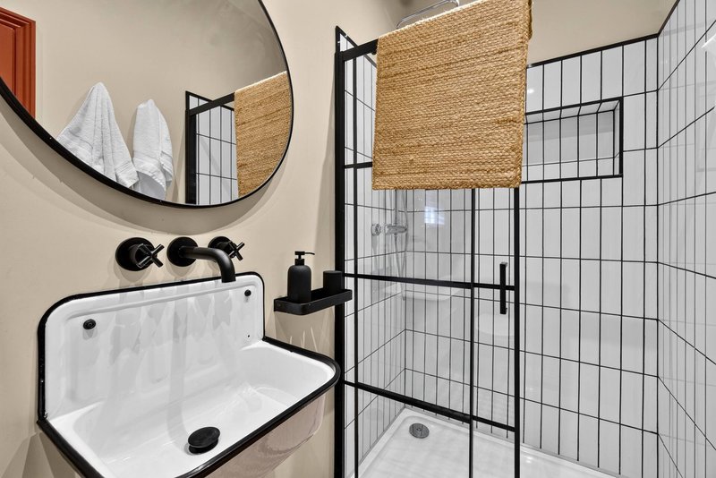 Modern bathroom with wall-mounted sink, round mirror, black fixtures and tiled shower enclosure