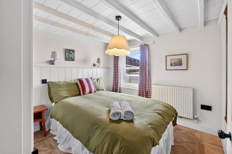 Bedroom with olive-green duvet, rolled towels, pendant light, and purple patterned curtains