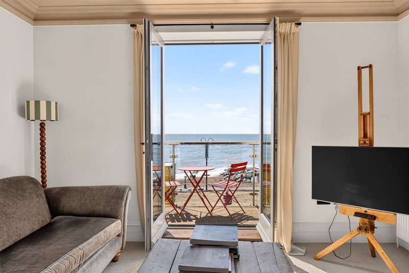 Modern living room with sofa, TV, and open glass doors to a balcony with sea view