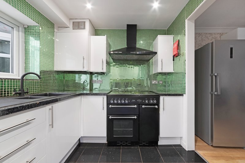 Modern kitchen with white cabinets, green tile backsplash, black range cooker and stainless steel fridge