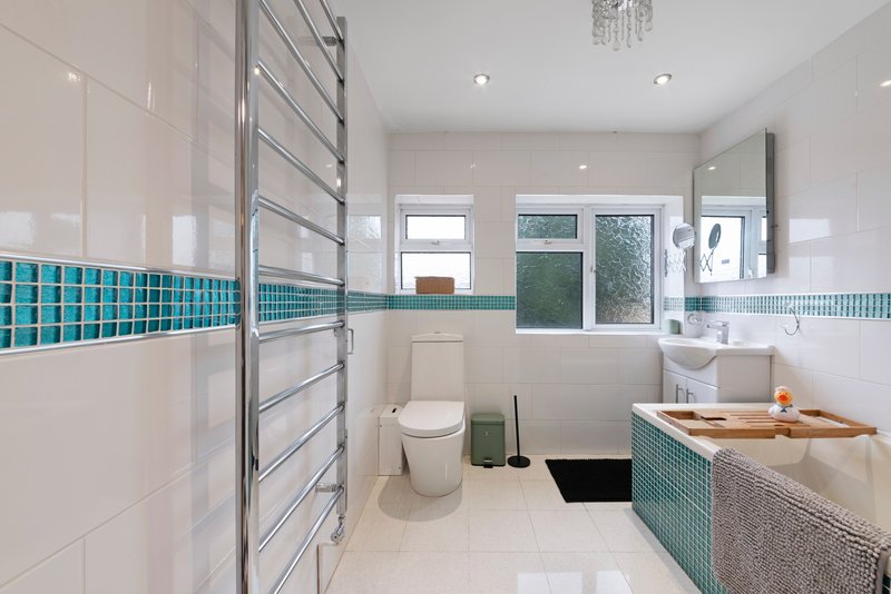 Modern bathroom with turquoise tile accents, walk-in shower, toilet, and vanity sink