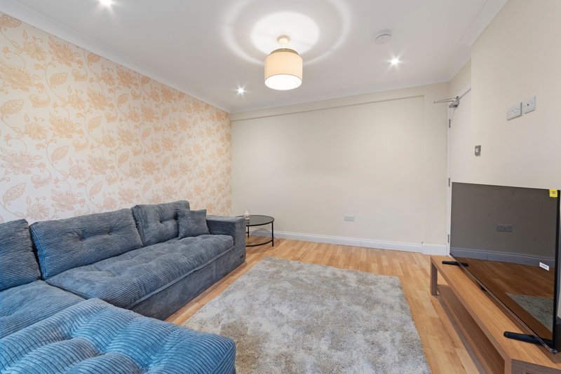 Living room with blue corner sofa, wooden flooring, patterned wallpaper and television