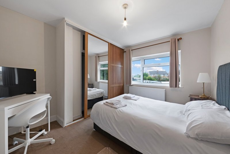 Bright bedroom with double bed, TV stand, desk chair, and countryside view through window