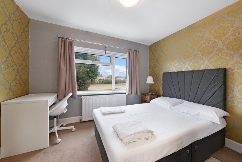 Bright bedroom with double bed, desk, patterned wallpaper and large window with countryside view