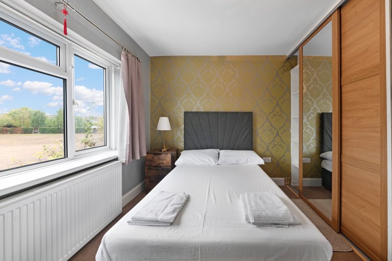 Bedroom with double bed, mirrored wardrobe, patterned wallpaper and large window with countryside view