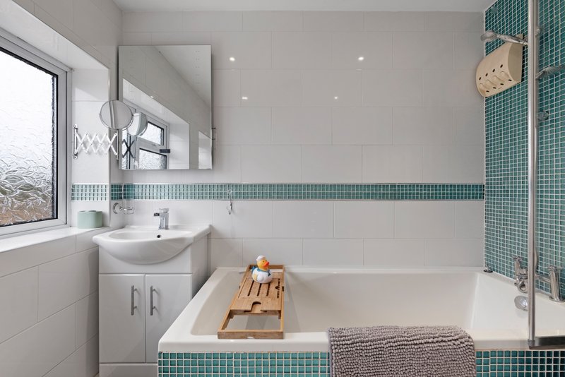 Modern bathroom with white sink, bathtub, teal tile accents and window