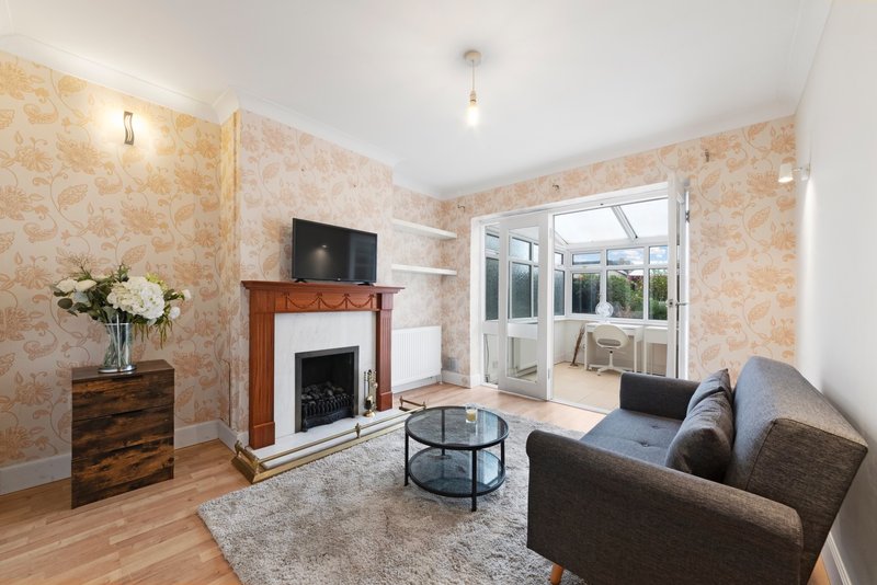 Living room with fireplace, grey sofa, wooden floor, patterned wallpaper and glass doors to garden