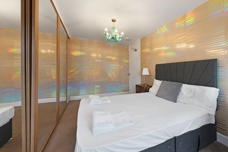 Modern bedroom with double bed, dark headboard, white bedding, ensuite shower room and chandelier