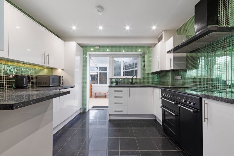Modern kitchen with white cabinetry, green tile backsplash, black appliances and dark floor