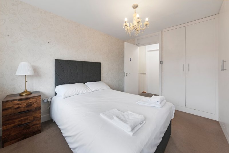 Modern bedroom with double bed, black headboard, wooden nightstand, chandelier, and built-in wardrobe