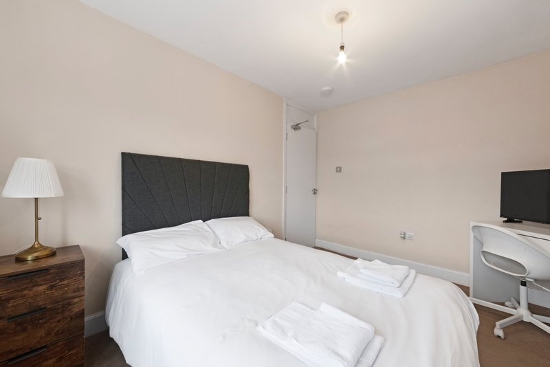 Bedroom with double bed, black headboard, white bedding, wooden nightstand and desk.
