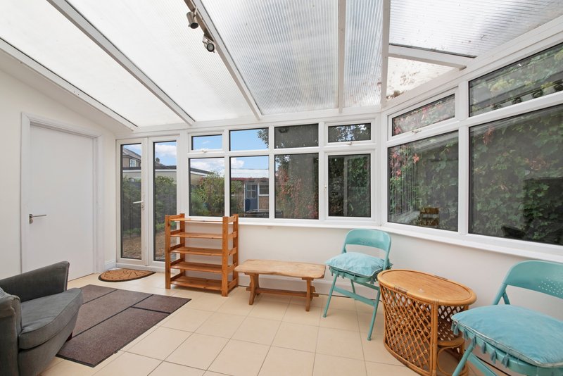 Bright conservatory with glazed roof, turquoise chairs, wooden furniture and garden views