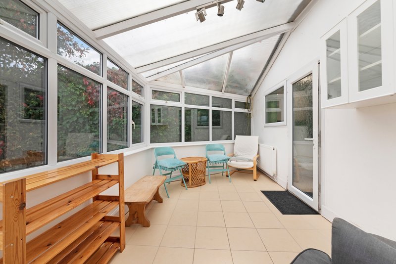 Bright conservatory with wooden shelving, blue chairs, tiled floor and large windows