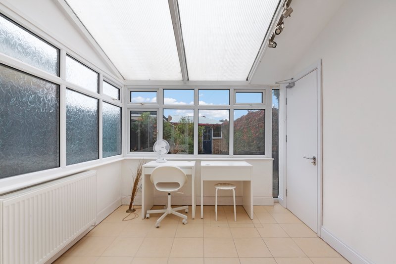 Bright conservatory with desk, chair, tiled floor and large windows overlooking garden
