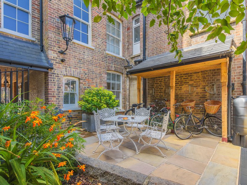 Brick courtyard with patio seating, flowering plants, bike storage, and glass extension doors