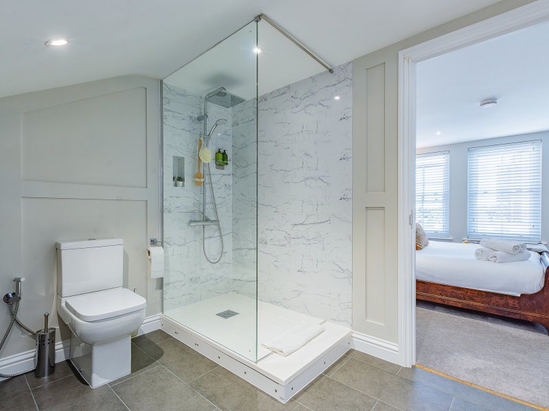 Modern bathroom with large walk-in shower, white marble tiles, toilet, and view to bedroom