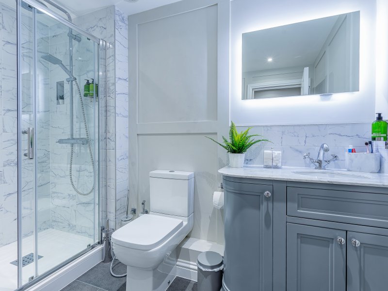 Modern bathroom with glass shower enclosure, gray vanity, white toilet and illuminated mirror