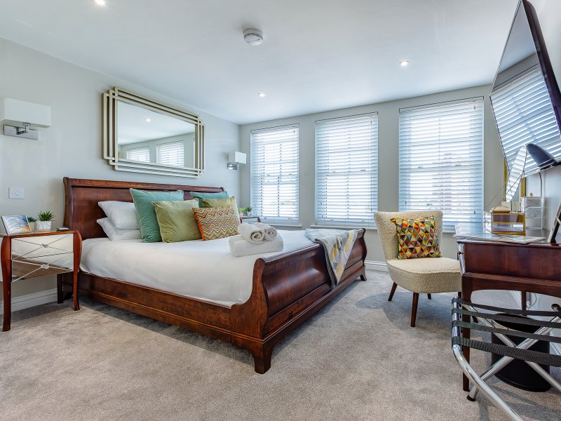 Spacious bedroom with wooden bed, decorative pillows, large windows with shutters, and contemporary furnishings