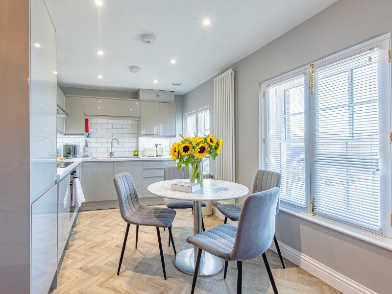 Modern kitchen-diner with white cabinetry, round table, grey chairs and sunflowers