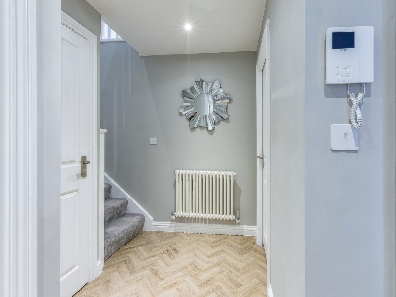 Hallway with herringbone wood flooring, white doors, decorative clock, radiator and wall-mounted controls