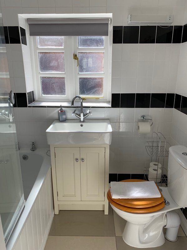 Clean bathroom with white sink vanity, toilet, bathtub, and window with black and white tile
