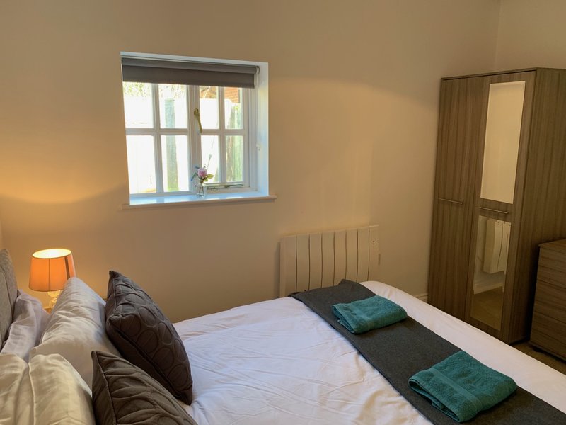Bright bedroom with double bed, dark headboard, window, orange lamp and wardrobe