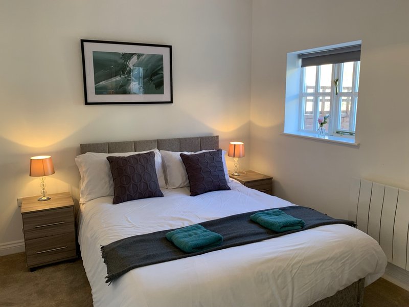 Modern bedroom with double bed, decorative pillows, bedside lamps, and framed landscape artwork
