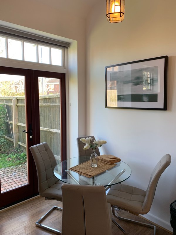 Dining area with round glass table, two brown chairs, framed artwork, and glass doors to garden
