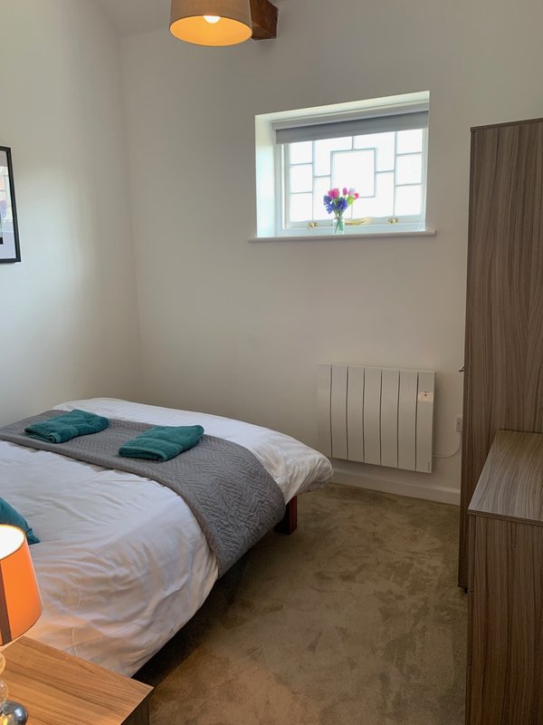 Small bedroom with single bed, white radiator, window with flower pot, wooden wardrobe