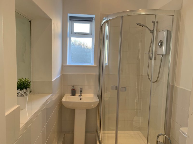 Modern bathroom with pedestal sink, shower enclosure, mirror and small window