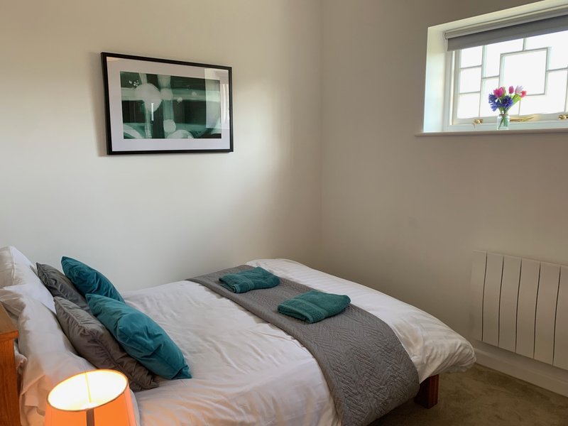 Bedroom with double bed, teal and grey pillows, framed wall art, and window with flowers