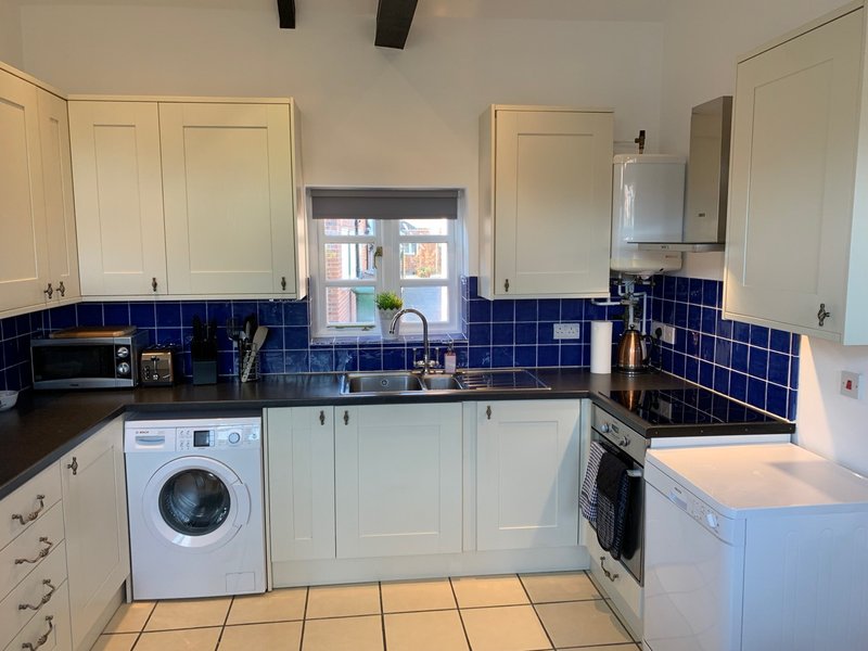 Modern kitchen with white cabinets, blue tile backsplash, washing machine and built-in appliances