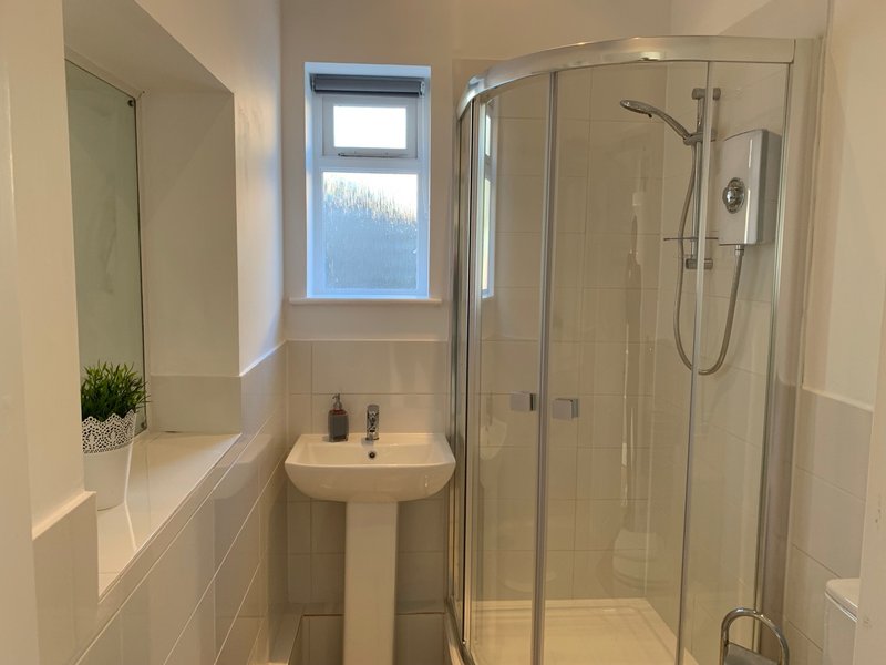 Modern bathroom with pedestal sink, shower enclosure, mirror and small window
