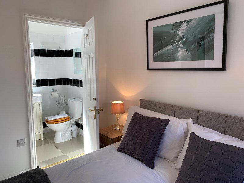Bedroom with double bed, bedside lamp, framed artwork, and ensuite bathroom visible through open door