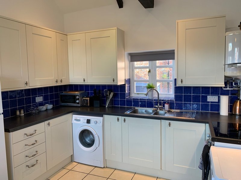 Modern kitchen with cream cabinets, blue tile backsplash, black worktops, washing machine and window
