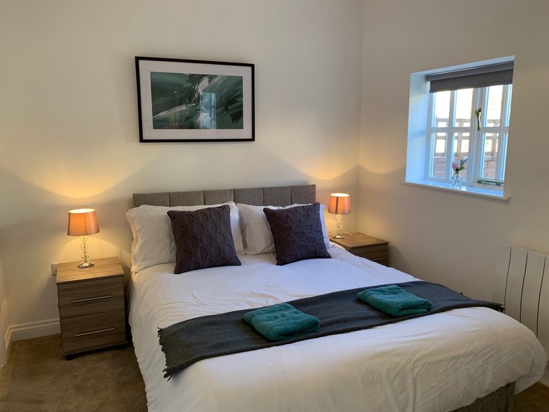 Modern bedroom with double bed, purple cushions, bedside lamps, framed artwork and window