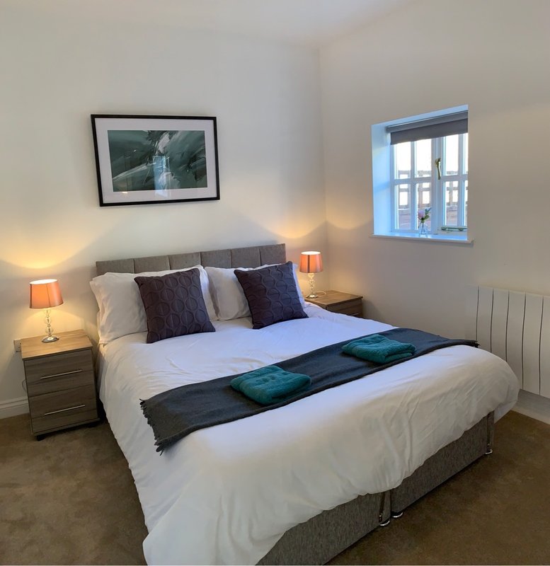 Modern bedroom with double bed, grey headboard, two bedside tables with lamps, and framed artwork